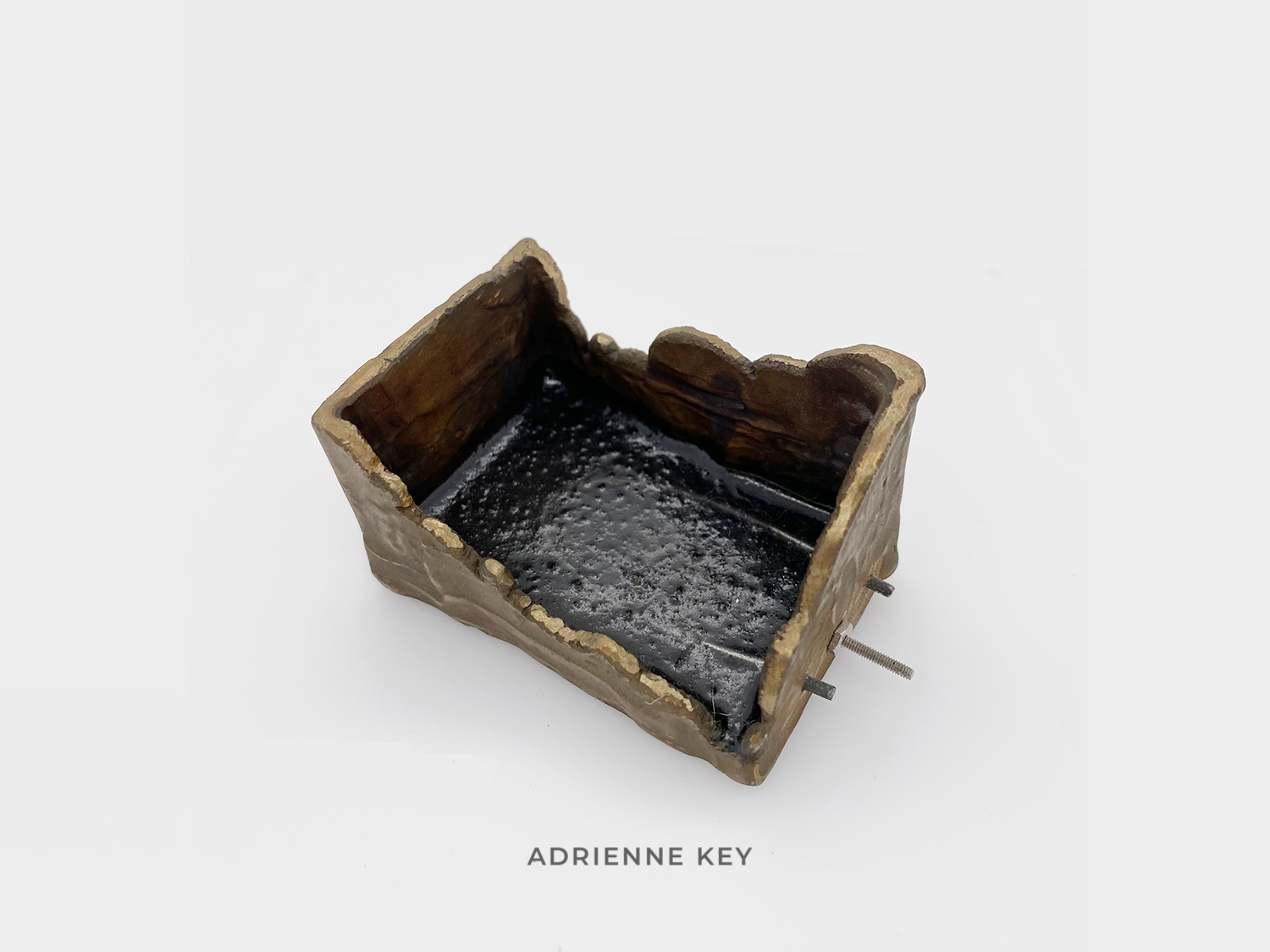 Sculpture of an organic bronze box filled with resin and a bent wire tube with screws protruding out