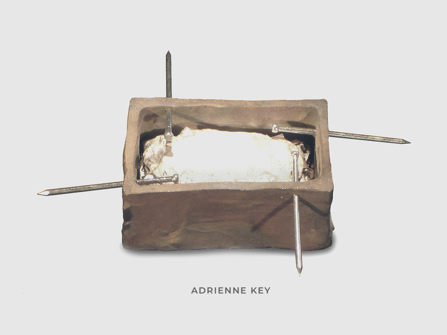 Sculpture of a bronze box filled with layers of melted aluminum with steel nails protruding out