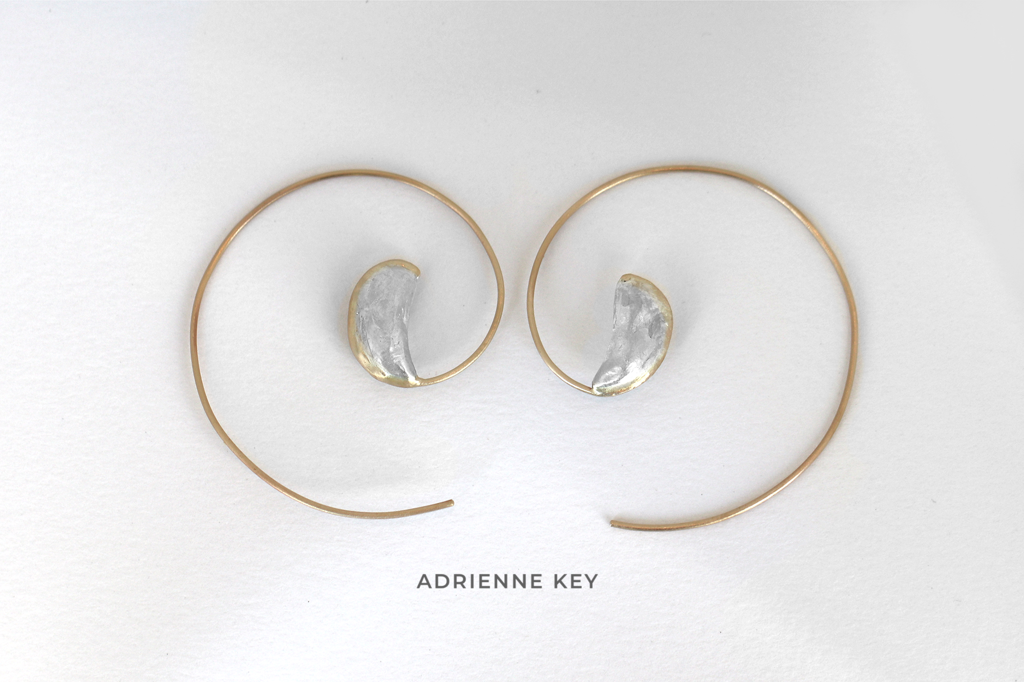 Cast sterling silver seed pods with 14k yellow gold swirl detail to form hoop earrings