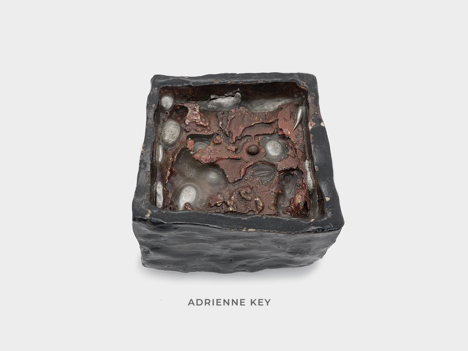 Sculpture of a black painted bronze box filled with melted copper mesh fused to vitreous enamel sunken in paraffin wax with melted balls of aluminum