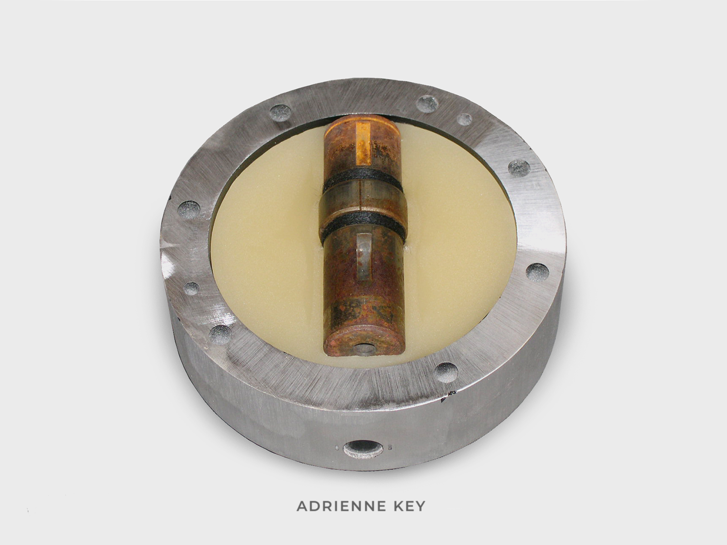 Sculpture of a circular found aluminum object and filled with beeswax with a sunken rusted steel found object wrapped in black cotton