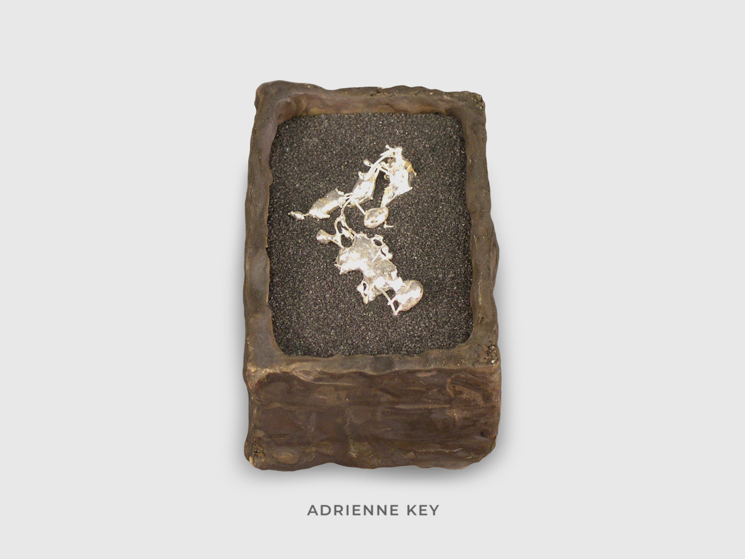 Sculpture of a bronze box filled with black sand and a melted organic shaped piece of fine silver