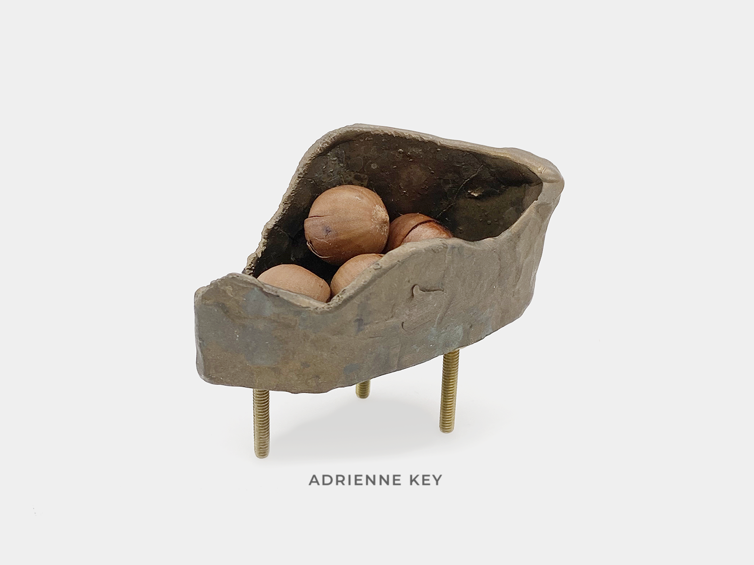 Sculpture of an organic bronze container on brass legs filled with hazelnuts