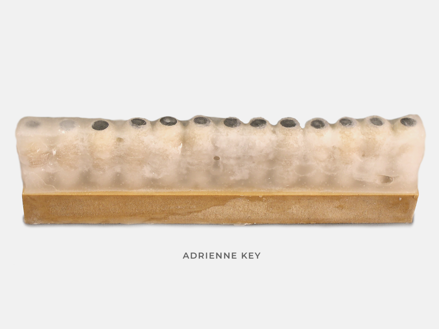 Sculpture of cotton wrapped nails hammered into a wood base in a row and coated in wax