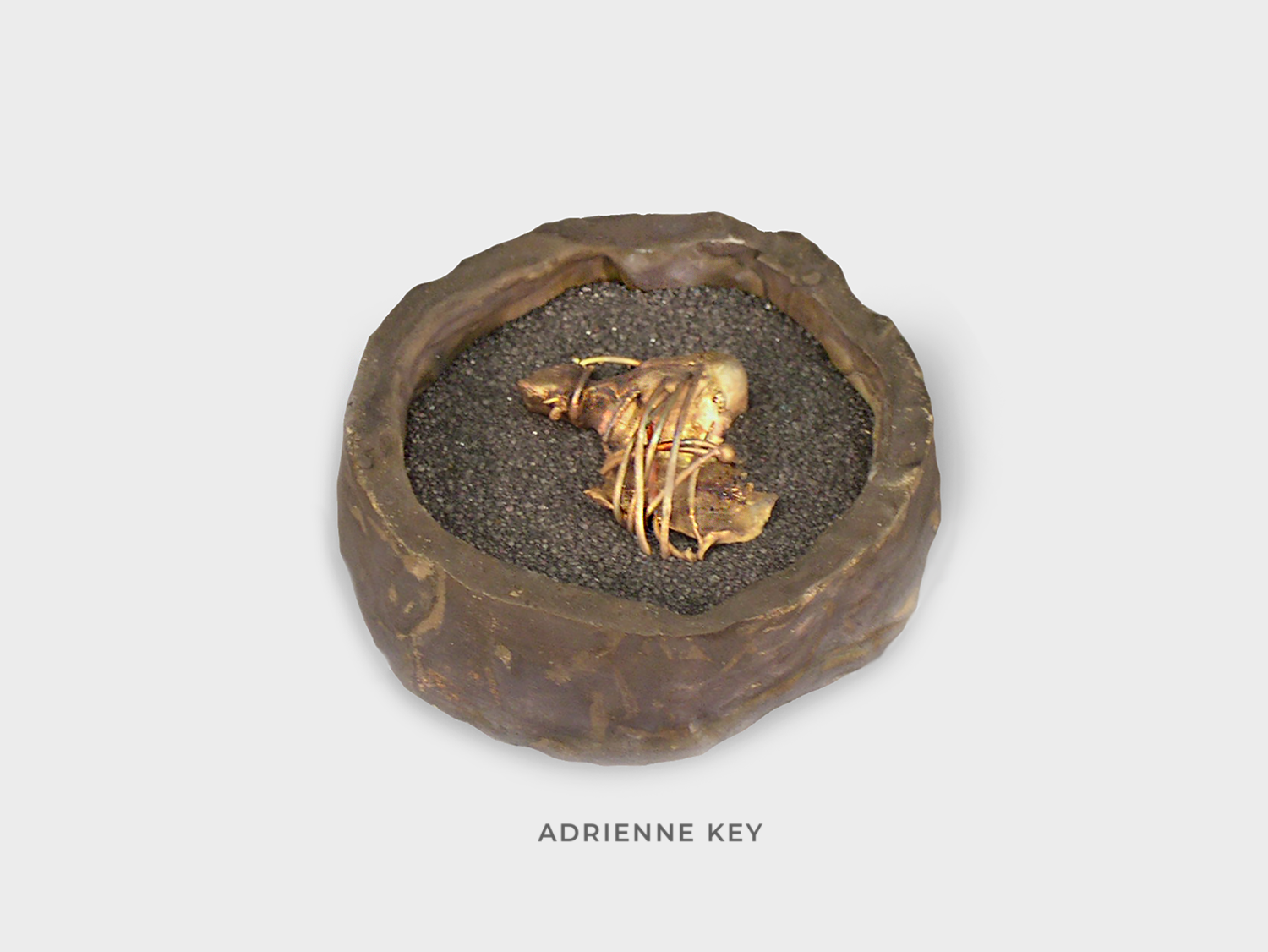 Sculpture of a round bronze box filled with black sand and a melted copper form