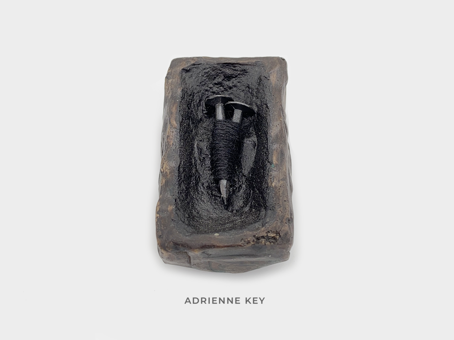 Sculpture of a bronze box filled with tar and two sunken steel nails bound together with black cotton string