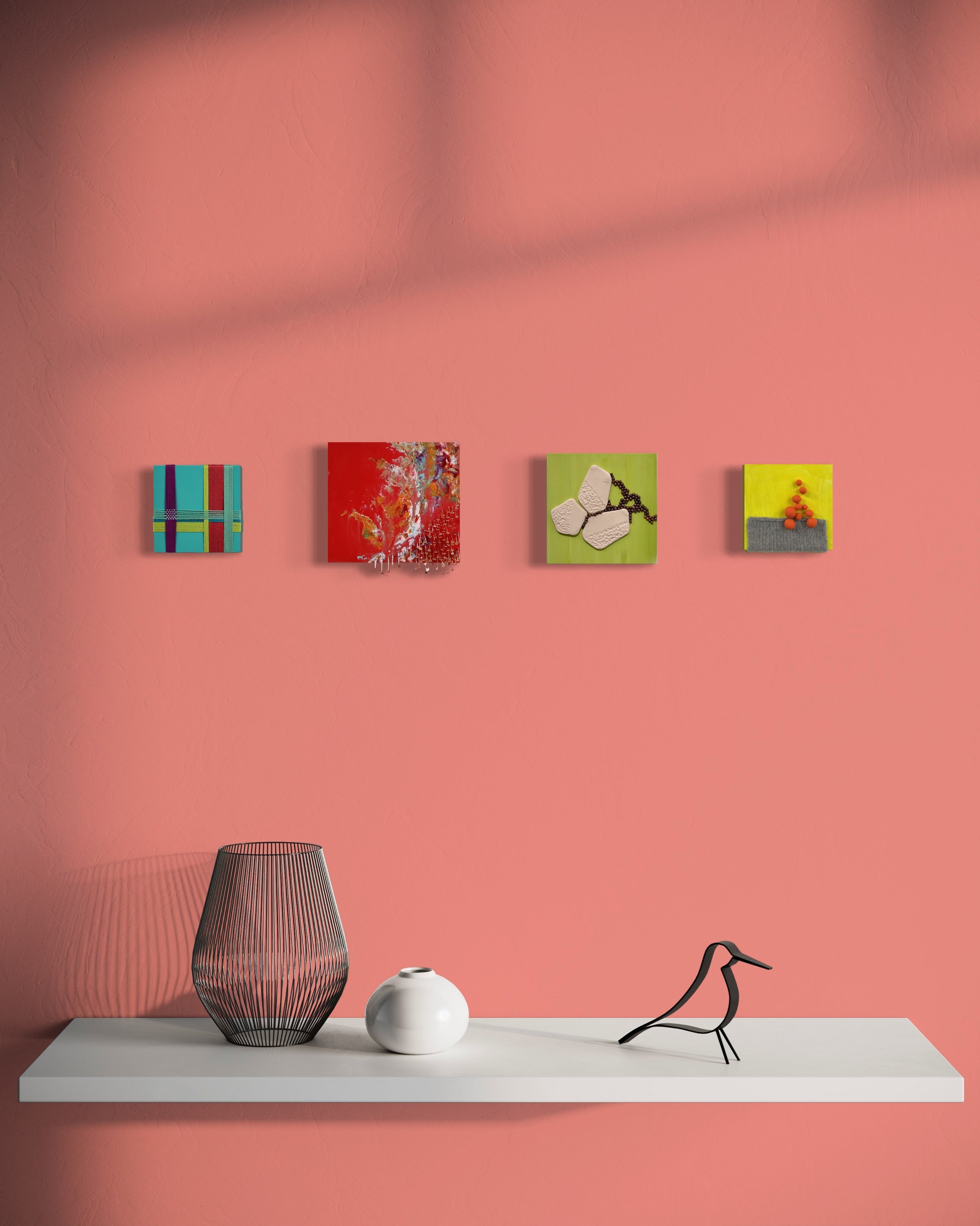 Four artworks displayed in a horizontal row on a pink wall above a shelf